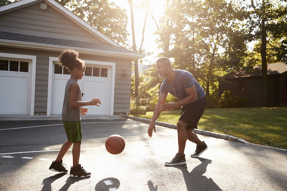 Father And Daughter Playing Basketball On Driveway At Home
