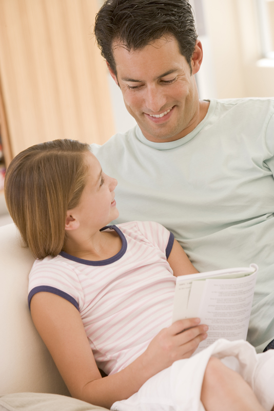 Father and daughter in living room reading book and smiling