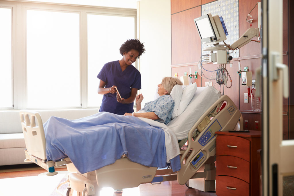 Hospital Nurse With Digital Tablet Talks To Senior Patient